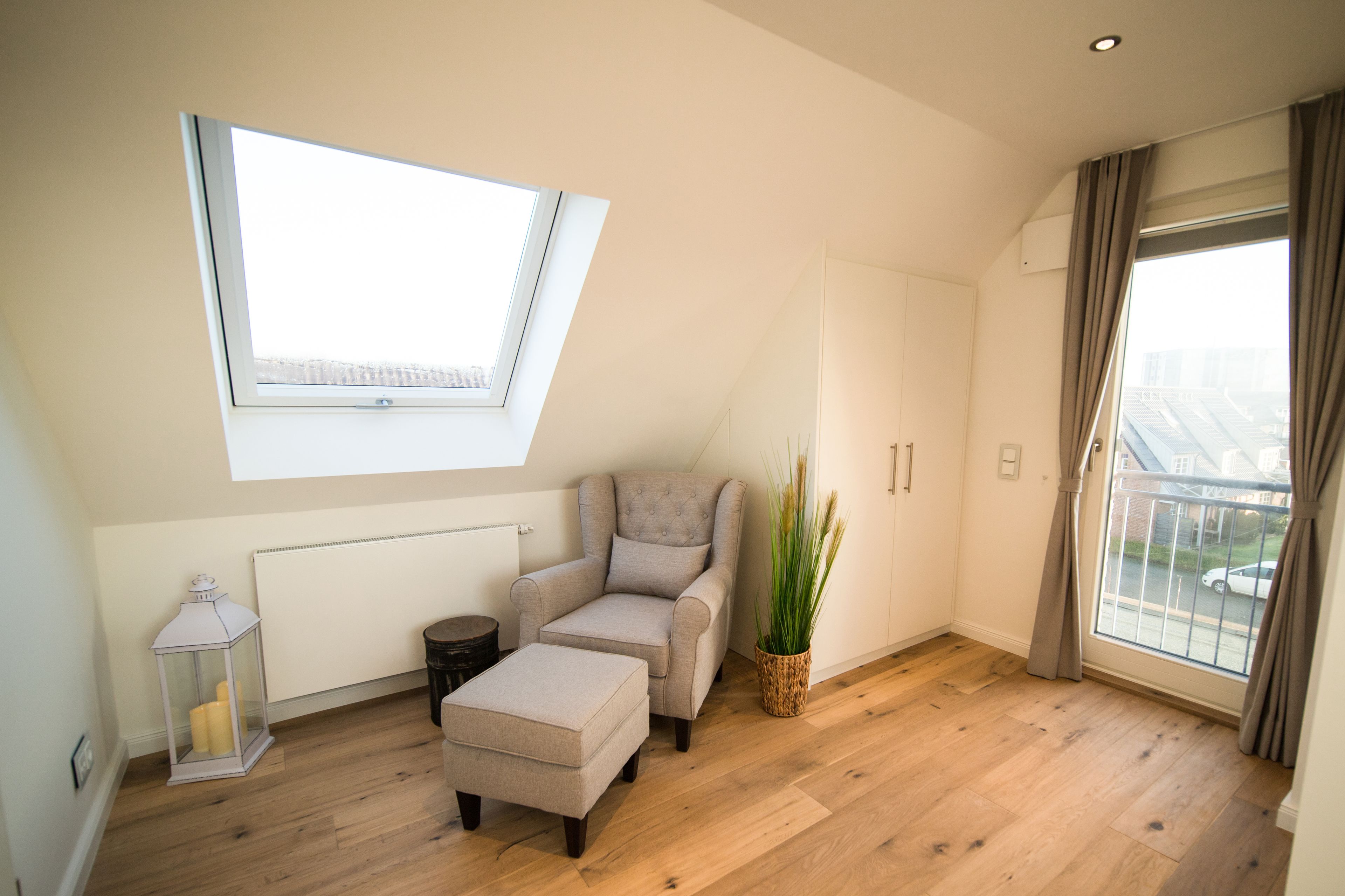 A modern living room with a skylight, a comfortable armchair, a small ottoman, a potted plant, and a view of the outside through a large window.
