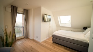 Un dormitorio moderno con cama, televisor, balcón y ventana.
