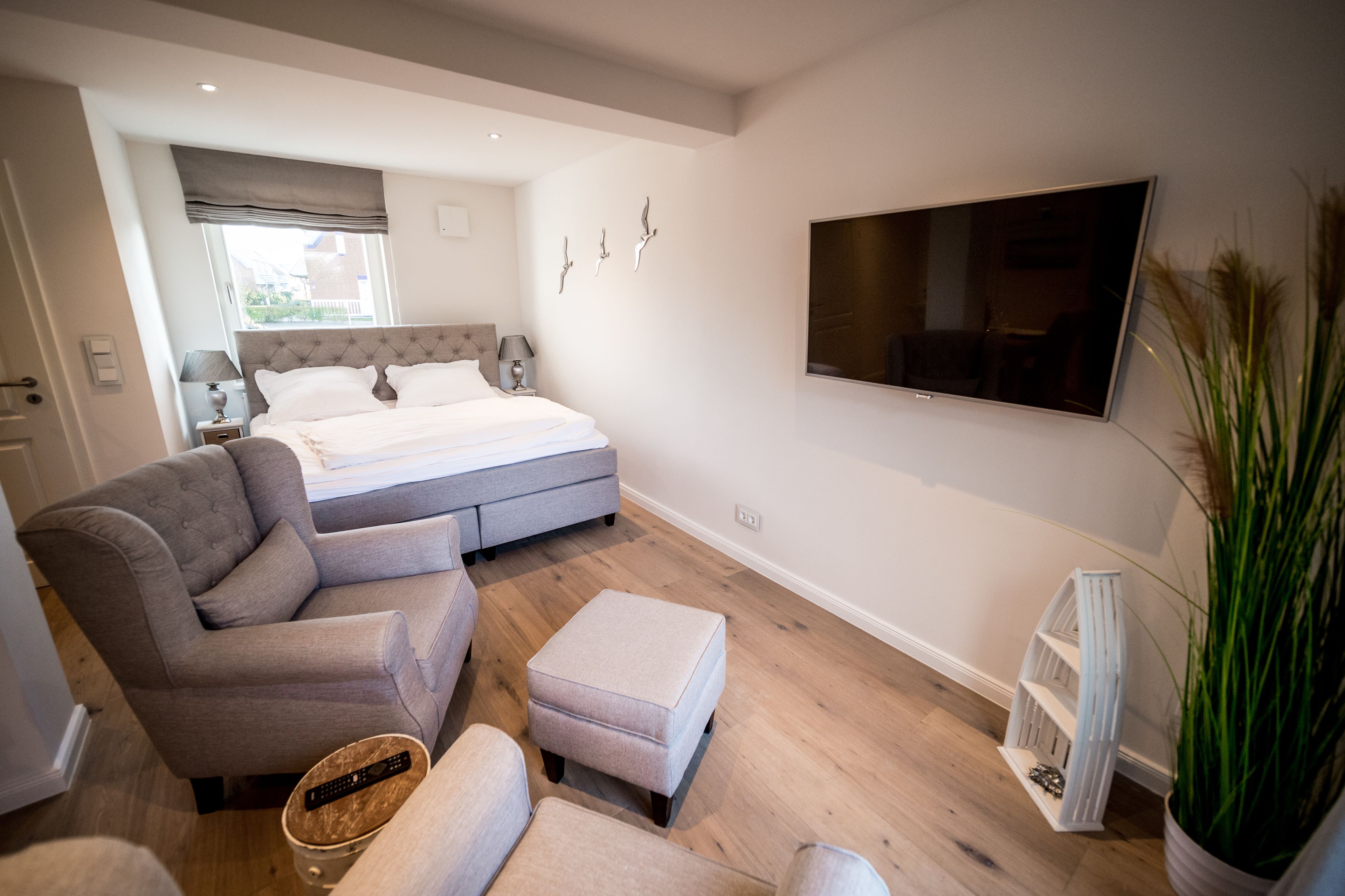 Une chambre à coucher moderne avec un lit, un canapé gris, une télévision et une plante en pot.