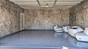 Eine geräumige Garage mit glatt poliertem Betonboden, einer weißen Tür und einer Sitzecke mit weißen, gepolsterten Stühlen.