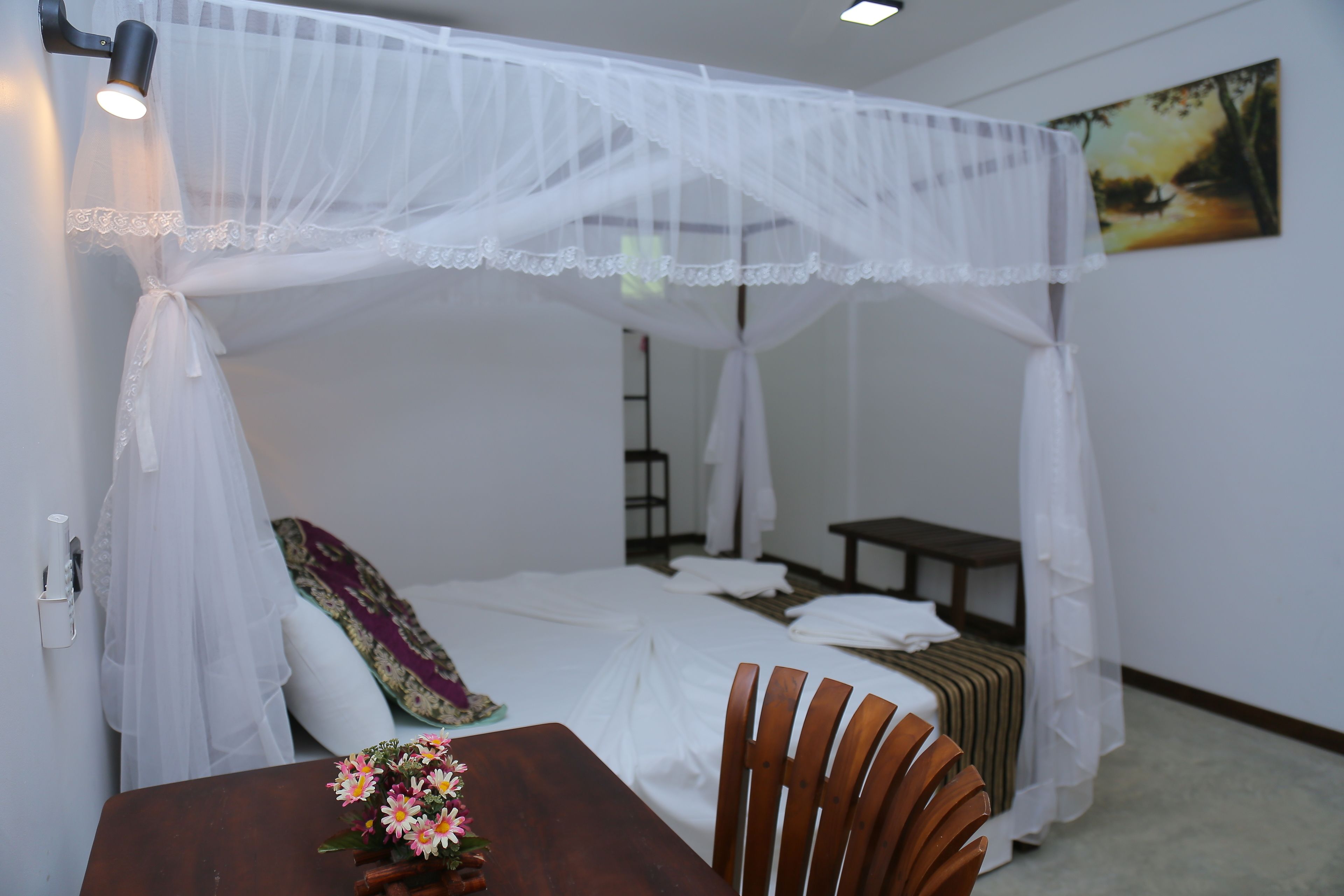 A bedroom with a canopy bed, a wooden table with a vase of flowers, and a painting on the wall.