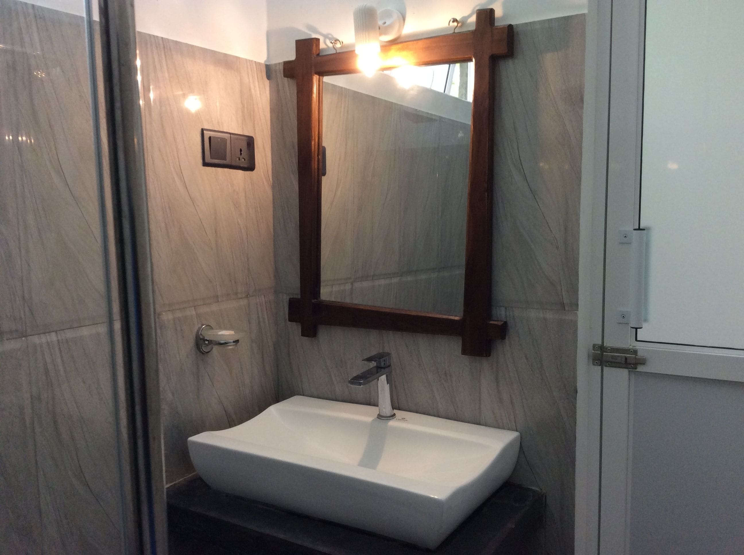 A bathroom with a white sink, a wooden-framed mirror, and a marble wall.