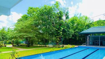 Una piscina con solárium de piedra, rodeada de exuberante vegetación y un área de estar cubierta.