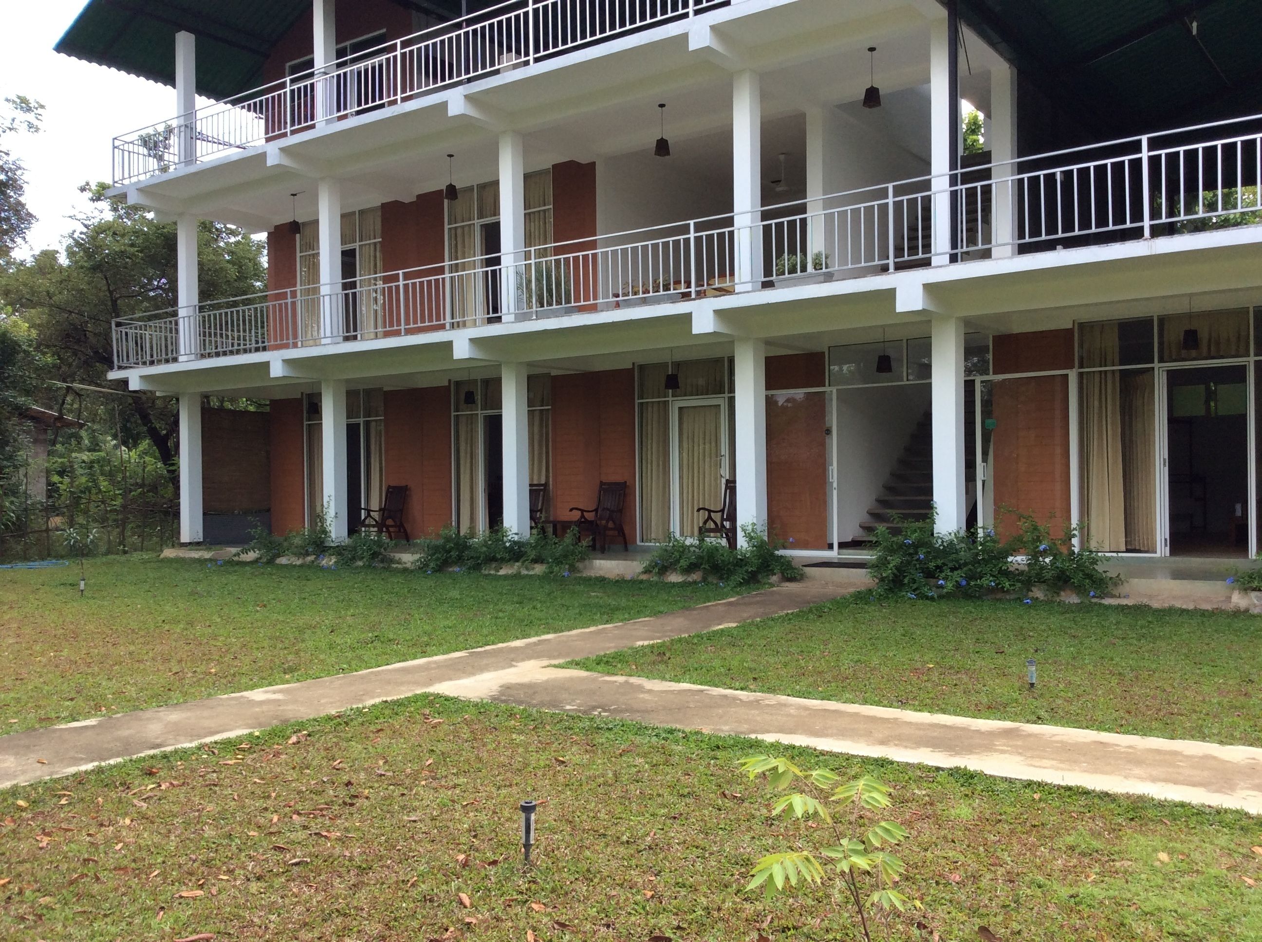 A two-story building with a balcony on the upper floor, a covered porch on the ground floor, and a pathway leading to the entrance.