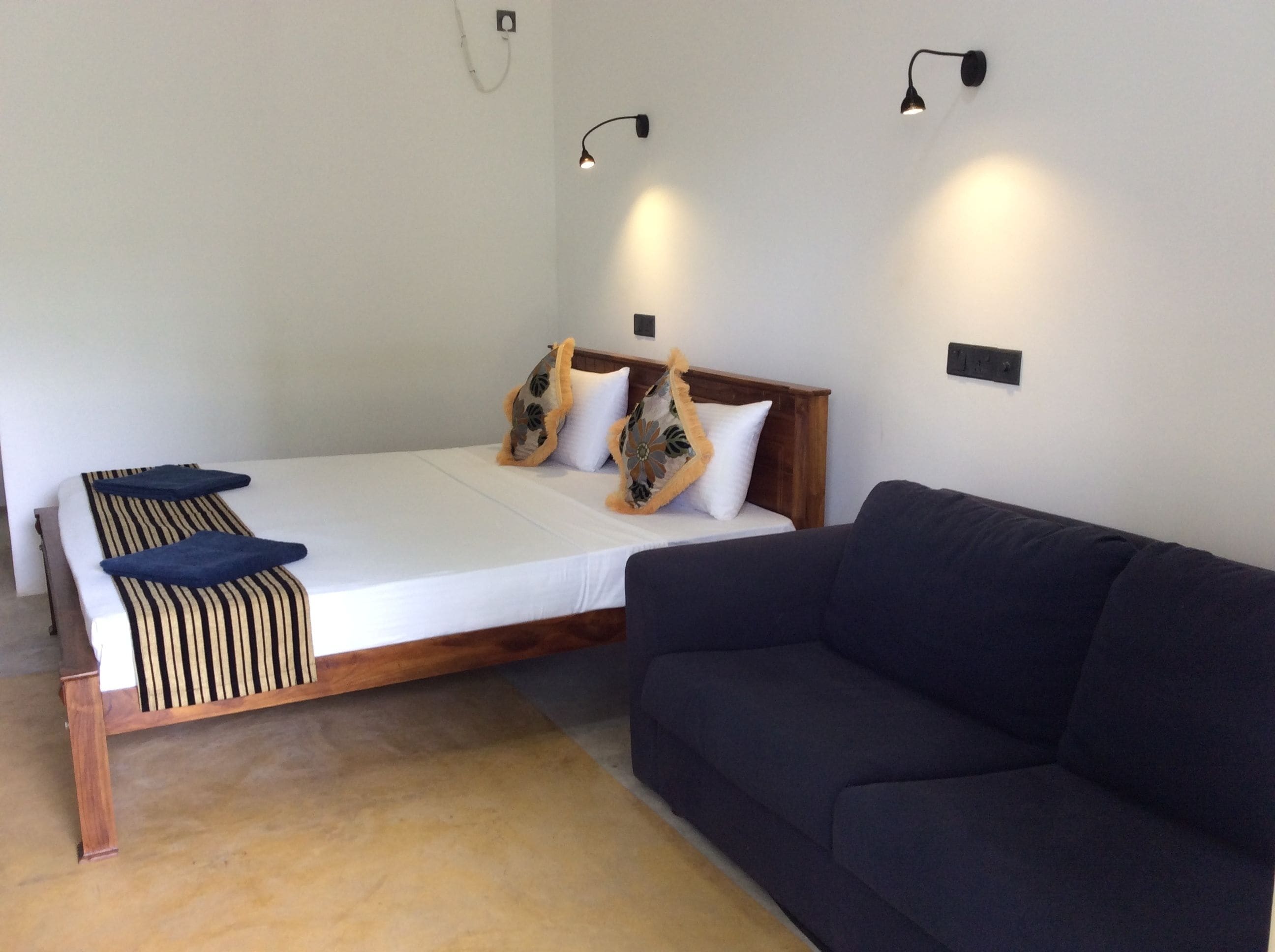 A bedroom with a bed, a dark sofa, and two wall-mounted lights.