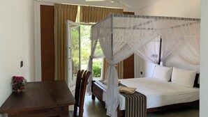 A bedroom with a bed, a wooden table, a chair, a ceiling fan, and a window with curtains. - Sigiriya Rock Hide (Sigiriya)