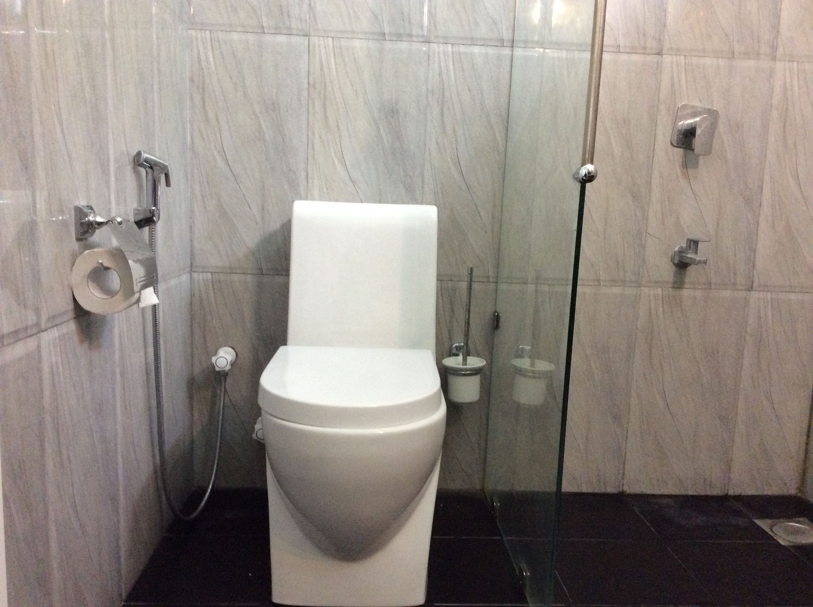 A modern bathroom with a white toilet, a glass shower enclosure, and a marble-tiled wall.
