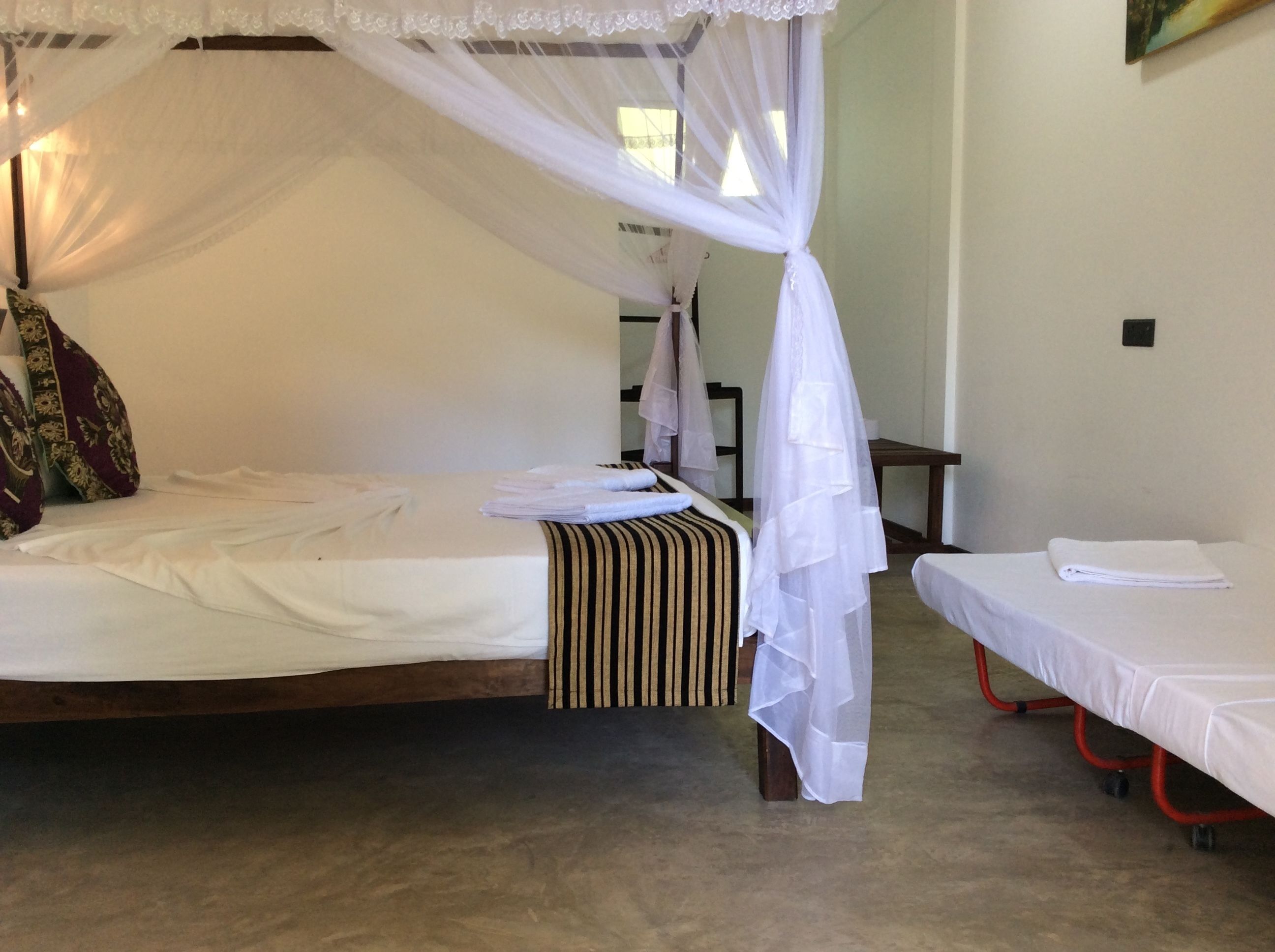 A room with a canopy bed, a smaller bed, and a nightstand with a lamp.