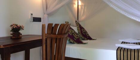 Una habitación con una cama bajo un dosel, una silla de madera, una mesita de noche y una lámpara fijada a la pared.