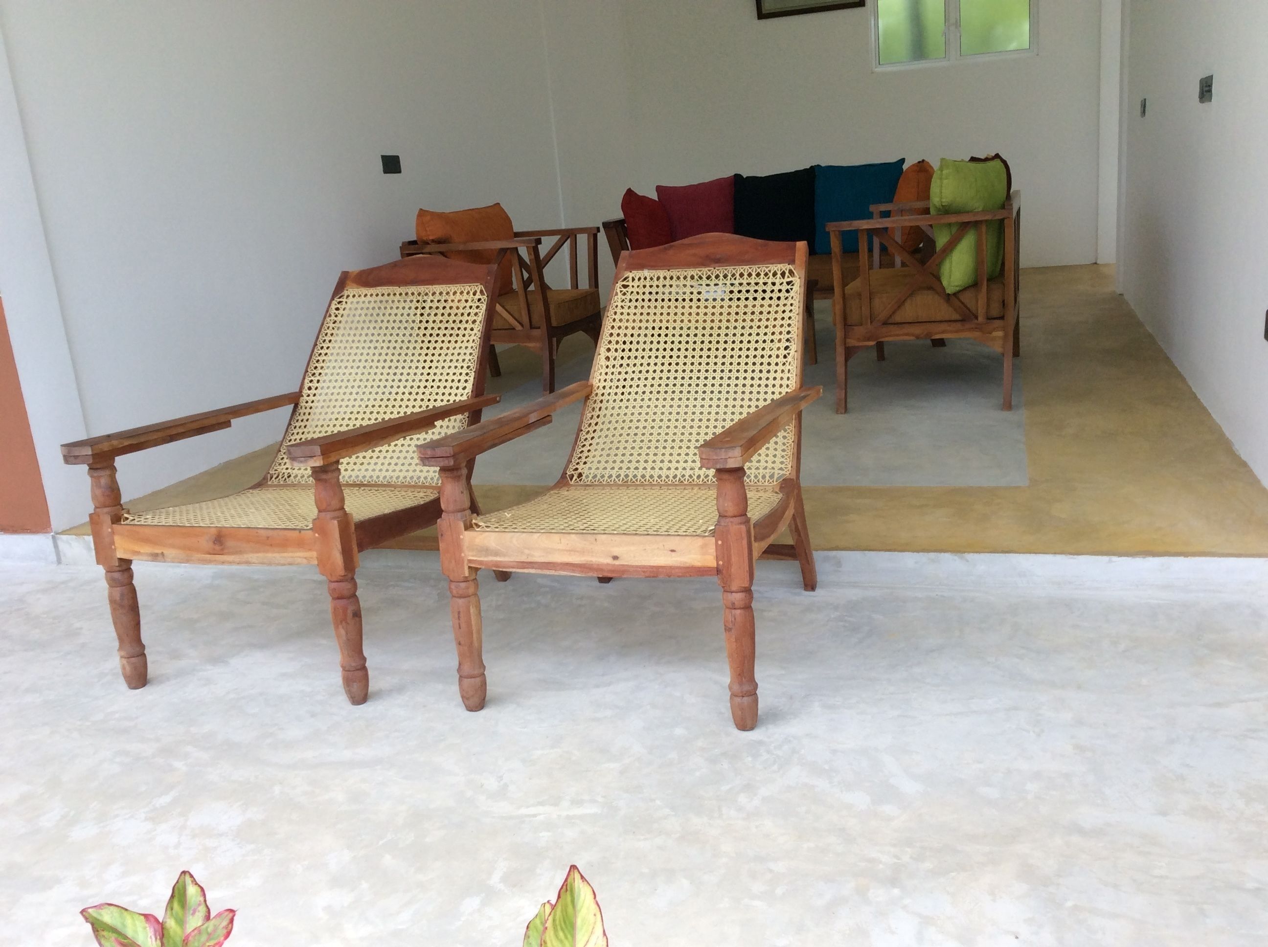 A room with two wooden chairs with woven seats and backs, a wooden table, and a sofa with cushions.
