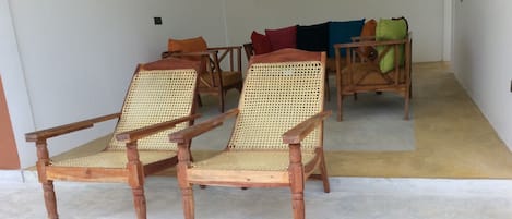 A room with two wooden chairs with woven seats and backs, a wooden table, and a sofa with cushions.