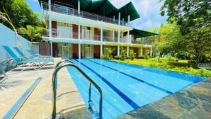 A swimming pool with a metal ladder, lounge chairs, and a building with balconies and a covered patio area. - Sigiriya Rock Hide (Sigiriya)