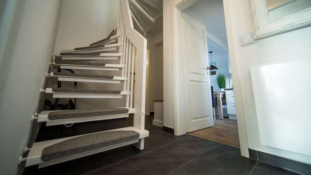 Una escalera moderna con barandilla y peldaños, que conduce a una habitación con puerta y una pequeña mesa con una planta.