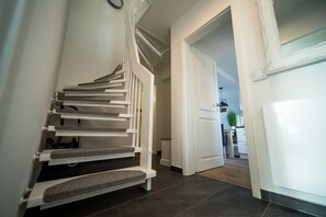 Una escalera moderna con barandilla y peldaños, que conduce a una habitación con puerta y una pequeña mesa con una planta.