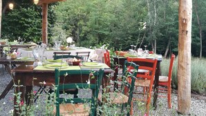 Un espacio de comedor al aire libre con mesas y sillas de madera, rodeado de follaje.