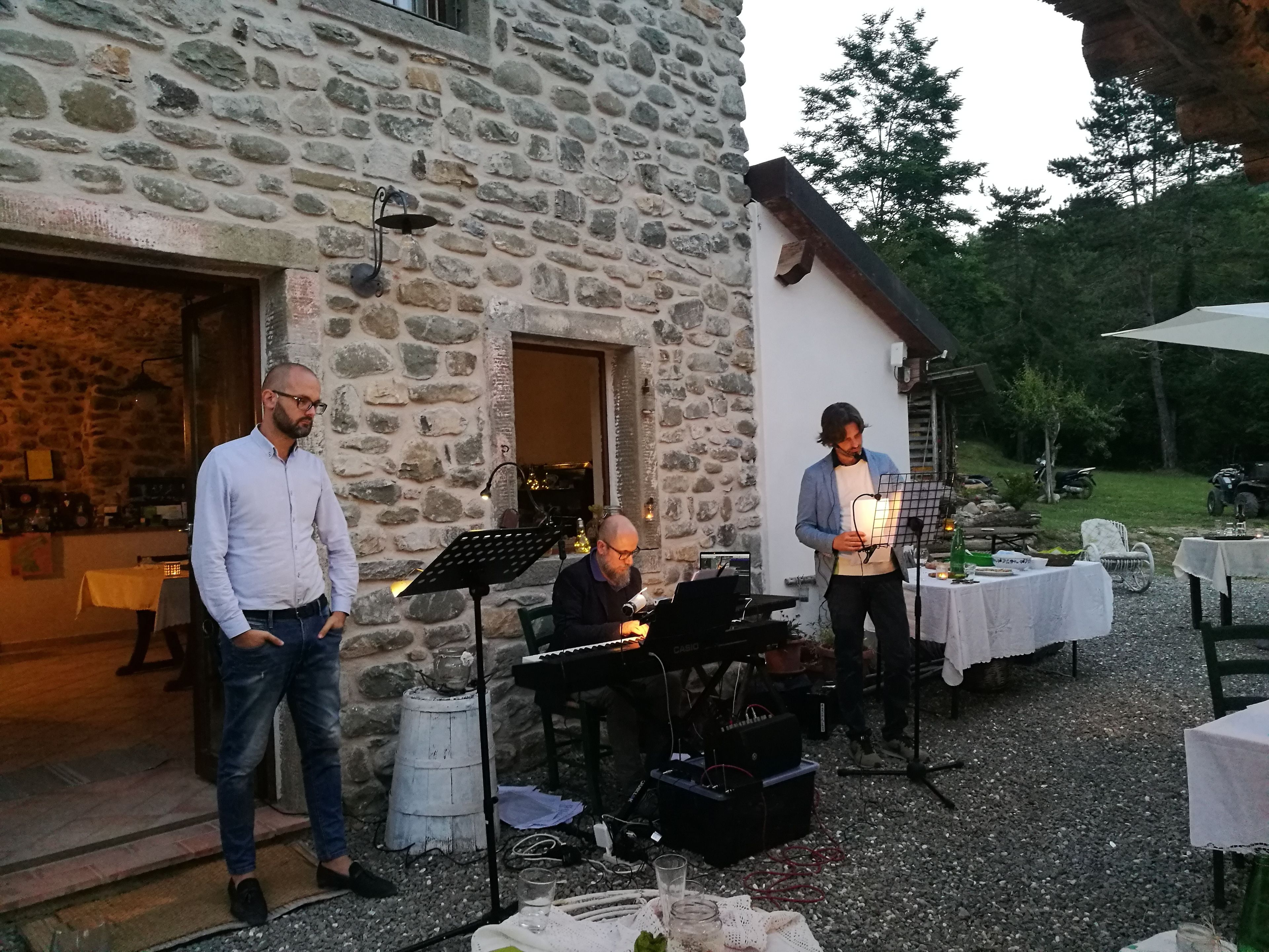 Ein Freiluft-Musikveranstaltungsbereich mit Steinmauern, einem Klavier und Tischen für das Publikum.