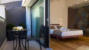 Ein modernes Schlafzimmer mit einem Bett, einem kleinen Tisch mit Stühlen und einer Glastür, die auf einen Balkon führt.