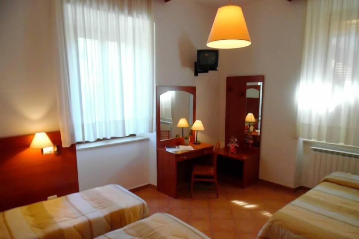 Une chambre d’hôtel avec deux lits, un bureau avec une chaise, un miroir et deux lampes fixées au mur.