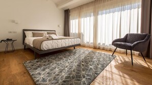 A bedroom with a bed, a chair, a rug, and a window with curtains. - Junior Suite with Terrace - A wisp of smoke (Catania)