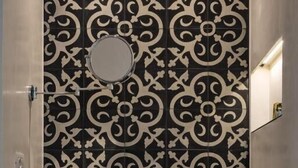 A bathroom with a black and white patterned wall, a round mirror, a wooden vanity, and two white towels. - Junior Suite with Terrace - A wisp of smoke (Catania)