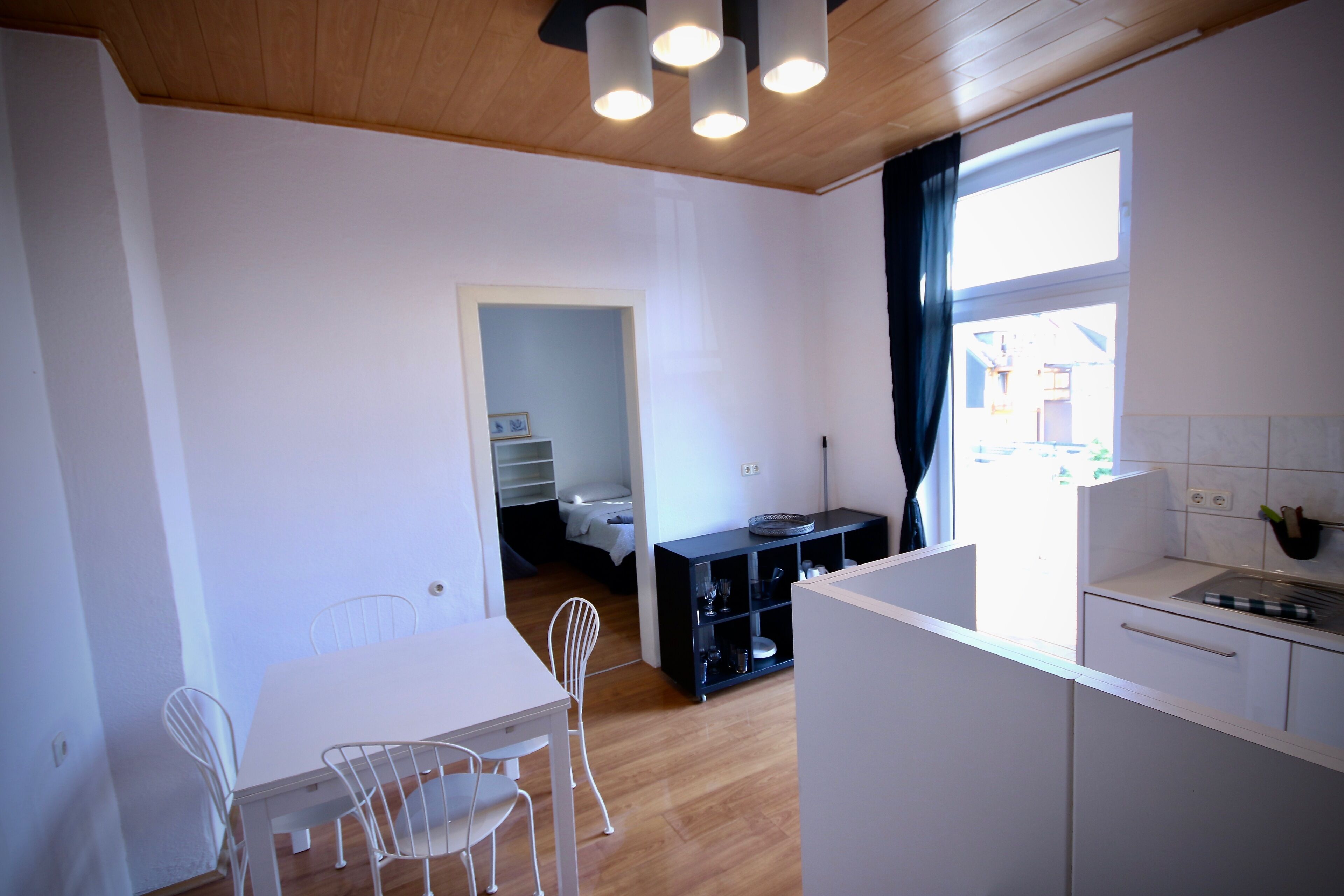 A compact kitchen with white cabinets, a dining table with chairs, and a window with curtains.
