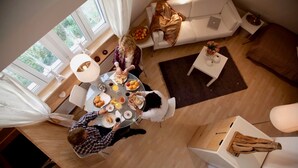 A dining area with a round table, white chairs, and a laptop on a white table. There is a sofa and a small table with a vase and fruit bowl in the background. - a-domo Apartments Oberhausen - Studio Apartments & Flats - short or longterm - single or grouptravel (Oberhausen)