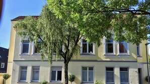 A two-story building with multiple windows and a tree in front. - a-domo Apartments Oberhausen - Studio Apartments & Flats - short or longterm - single or grouptravel (Oberhausen)
