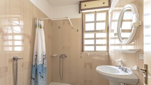 A bathroom with a toilet, shower, sink, and a window with a view.