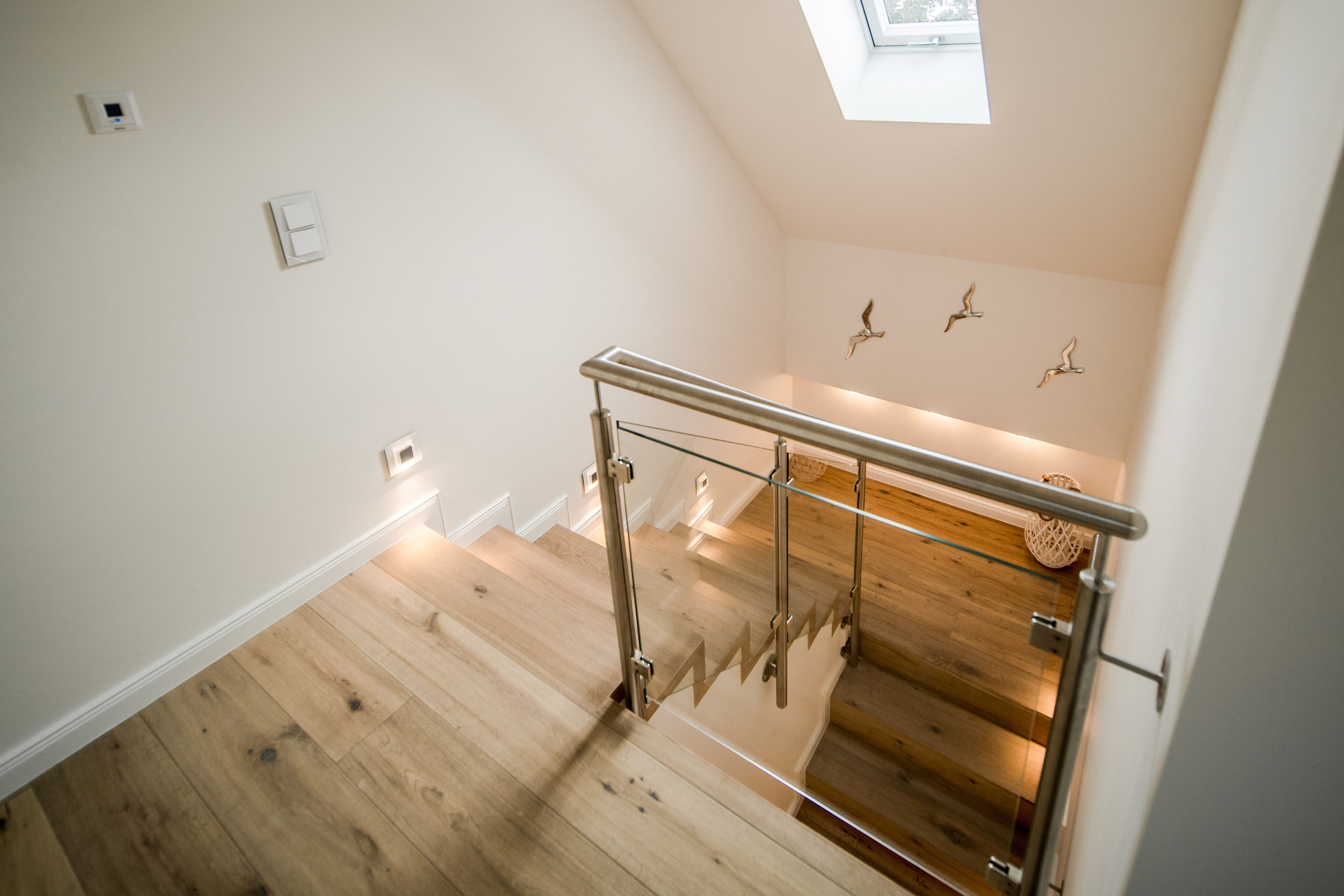 A modern staircase with glass railings and wooden flooring, leading to a room with a skylight and decorative wall art.