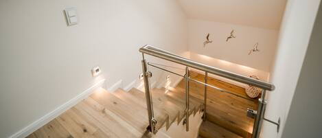 A modern staircase with glass railings and wooden flooring, leading to a room with a skylight and decorative wall art.