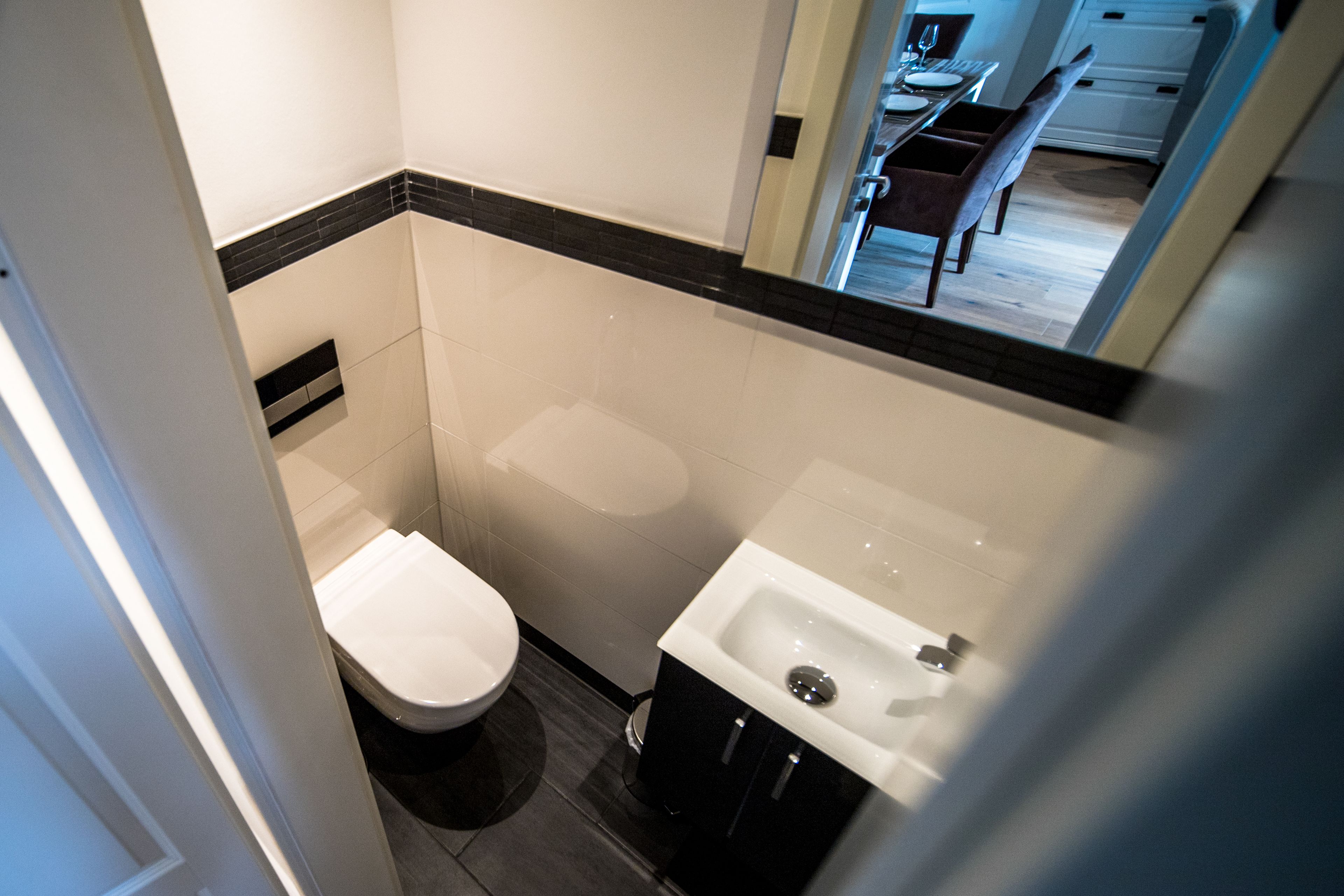 Un baño pequeño con inodoro, lavabo y un espejo que refleja un comedor.