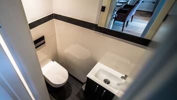 Un baño pequeño con inodoro, lavabo y un espejo que refleja un comedor.