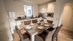 Une cuisine moderne avec des meubles blancs, une table à manger en bois pour quatre personnes et une vue sur l’extérieur.