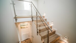 Un escalier avec des marches en bois et des rampes en métal, menant à un palier où se trouvent une porte et un tableau encadré.