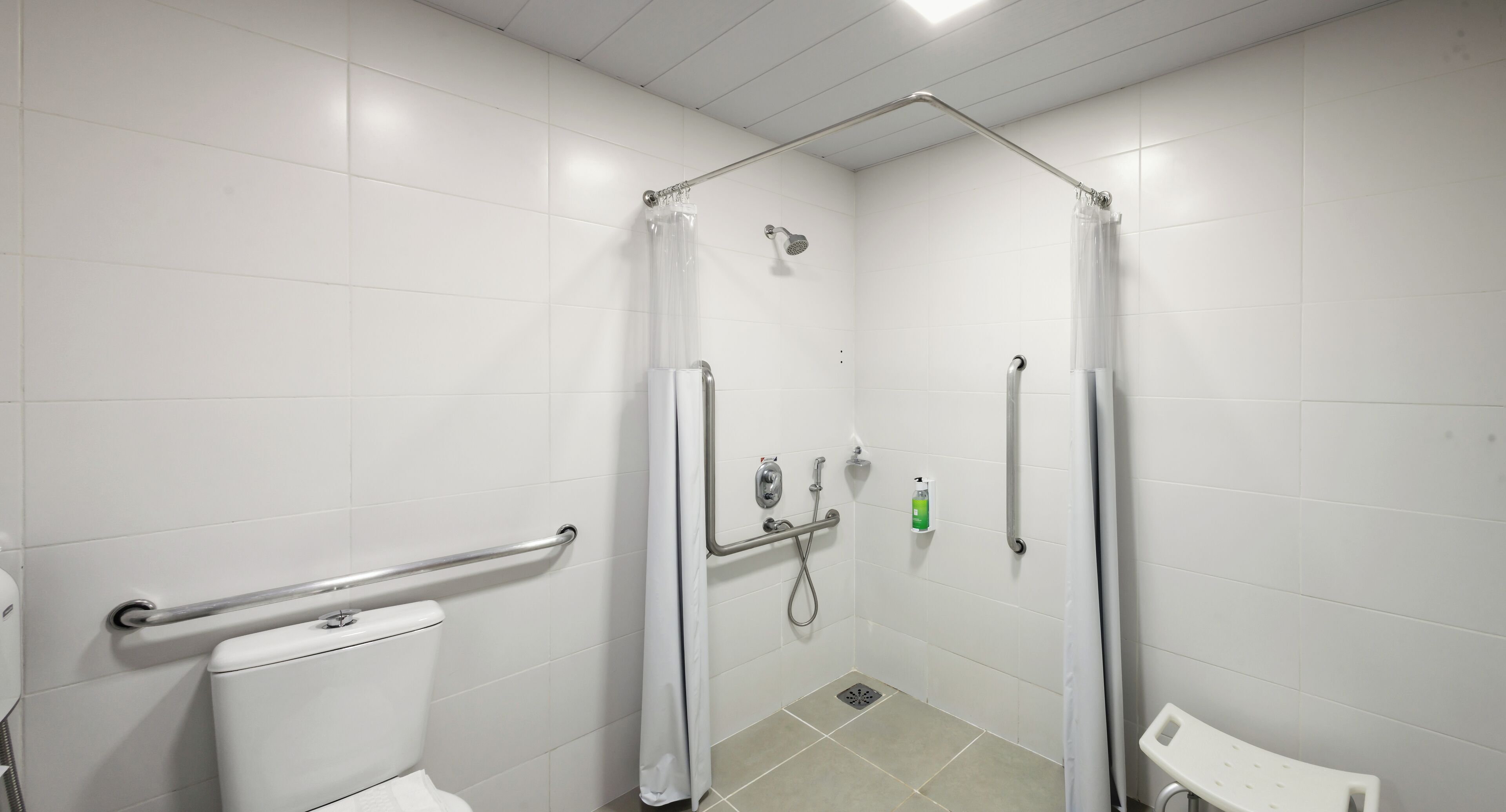 A wheelchair-accessible shower stall with grab bars, a toilet, and a bench.