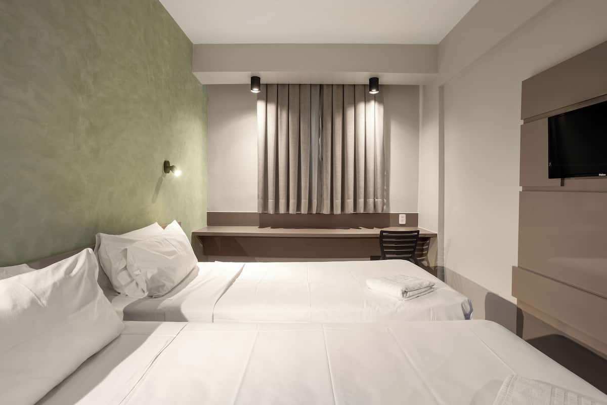 A hotel room with two beds, a flat-screen TV, a desk, and a window with curtains.