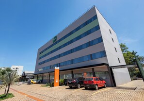 Um hotel moderno com telhado plano, vários andares e uma área de estacionamento com diversos carros.