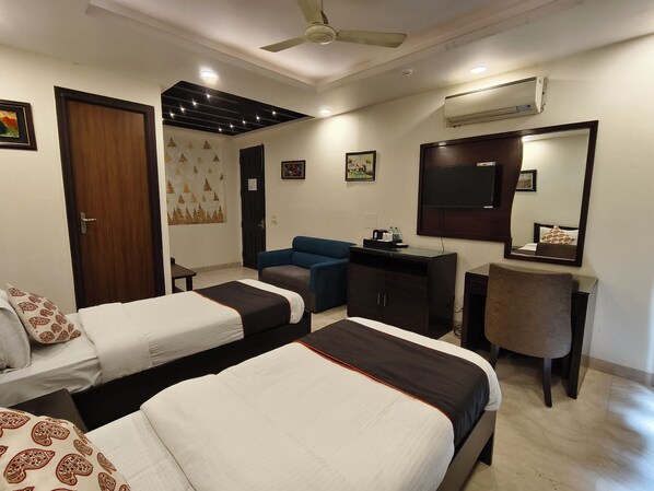 A hotel room with two beds, a desk, a chair, a wardrobe, a ceiling fan, and a large mirror.