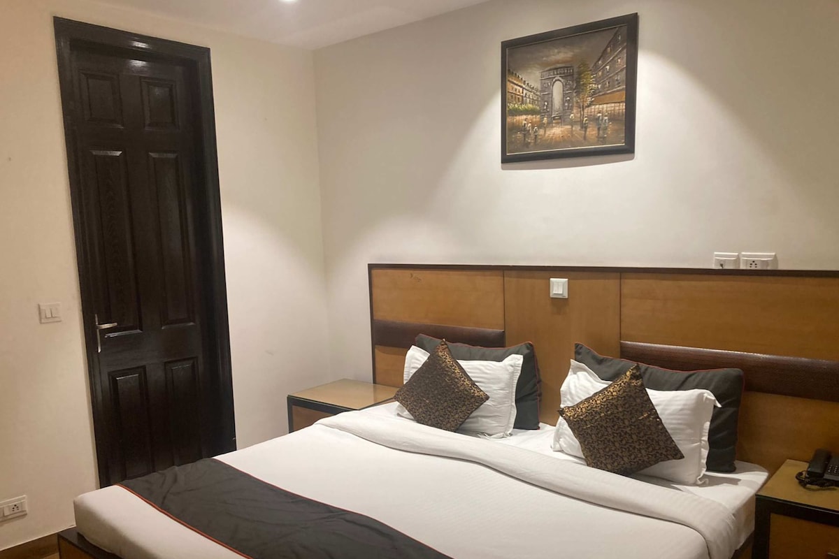 A hotel room with a bed, bedside tables, a painting on the wall, and a door.
