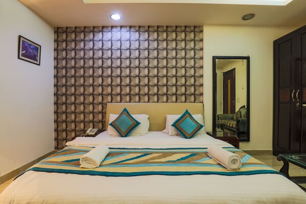 A hotel room with a large bed, a padded headboard, and a mirror on the wall.