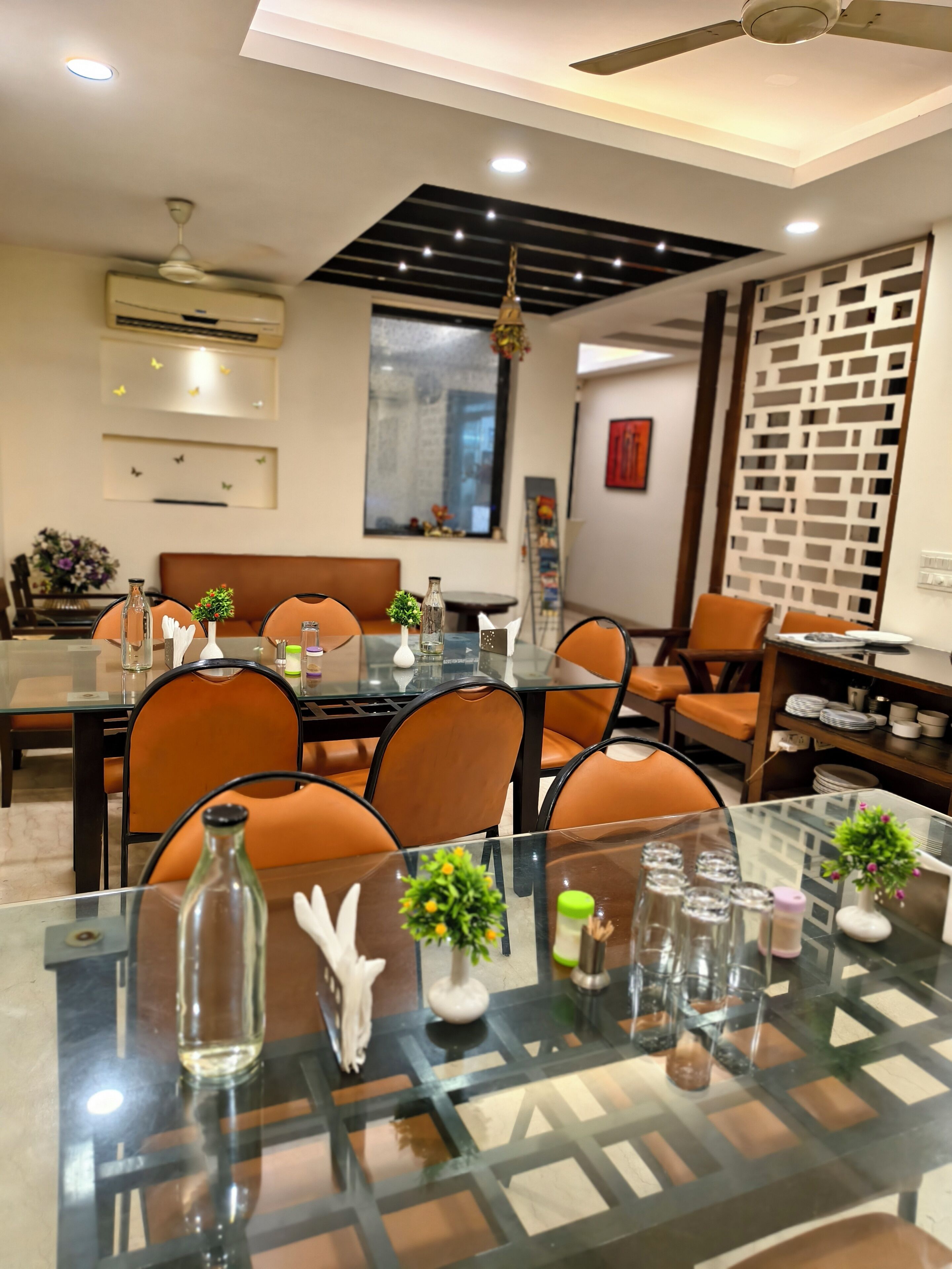 A modern dining area with glass tables, orange chairs, and decorative items.