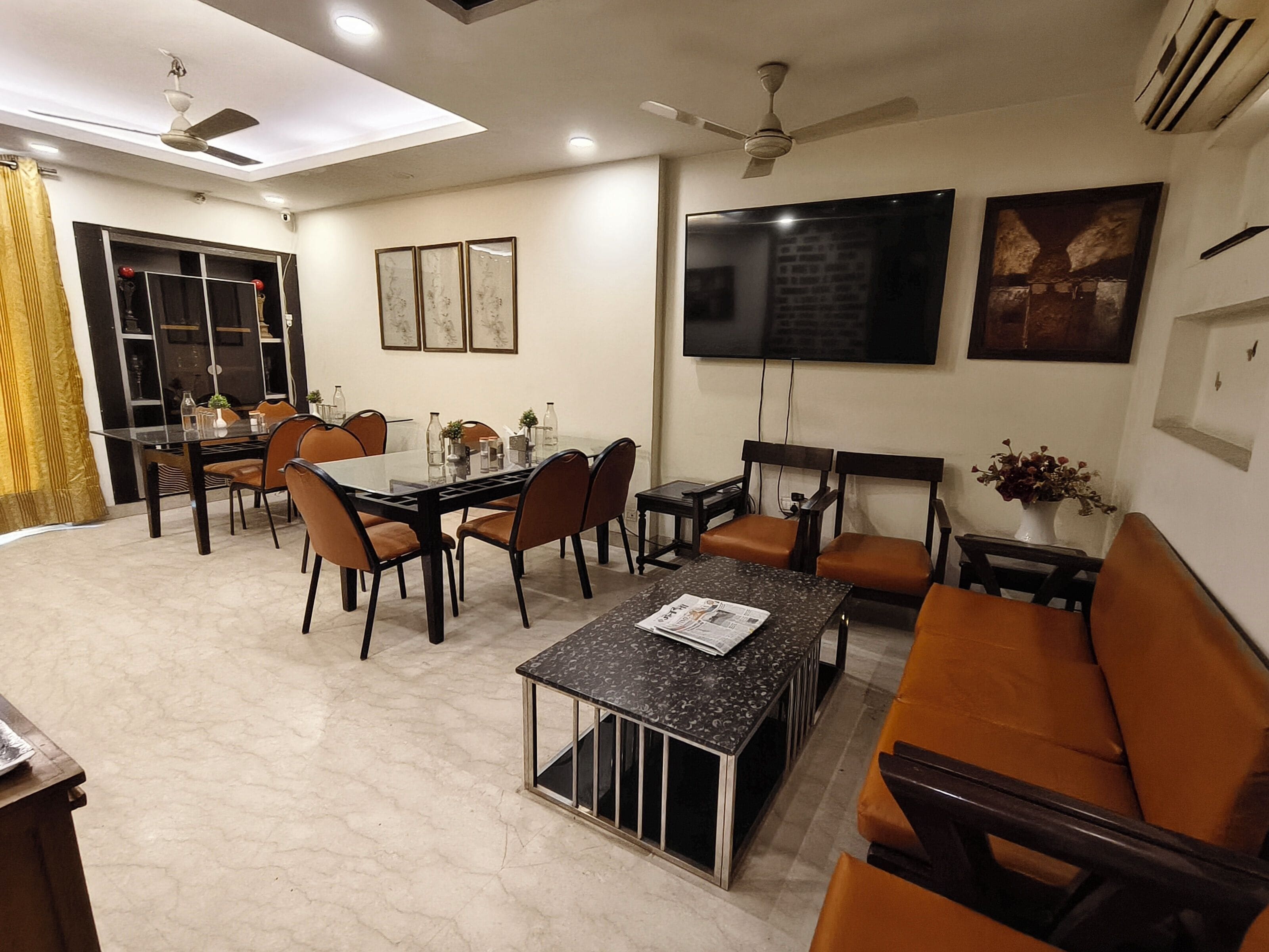 A modern living room with a dining area, featuring a flat-screen TV, comfortable seating, and a ceiling fan.