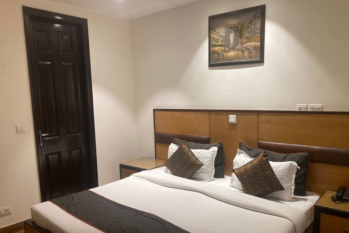 A hotel room with a large bed, a headboard, a nightstand, a telephone, and a painting on the wall.