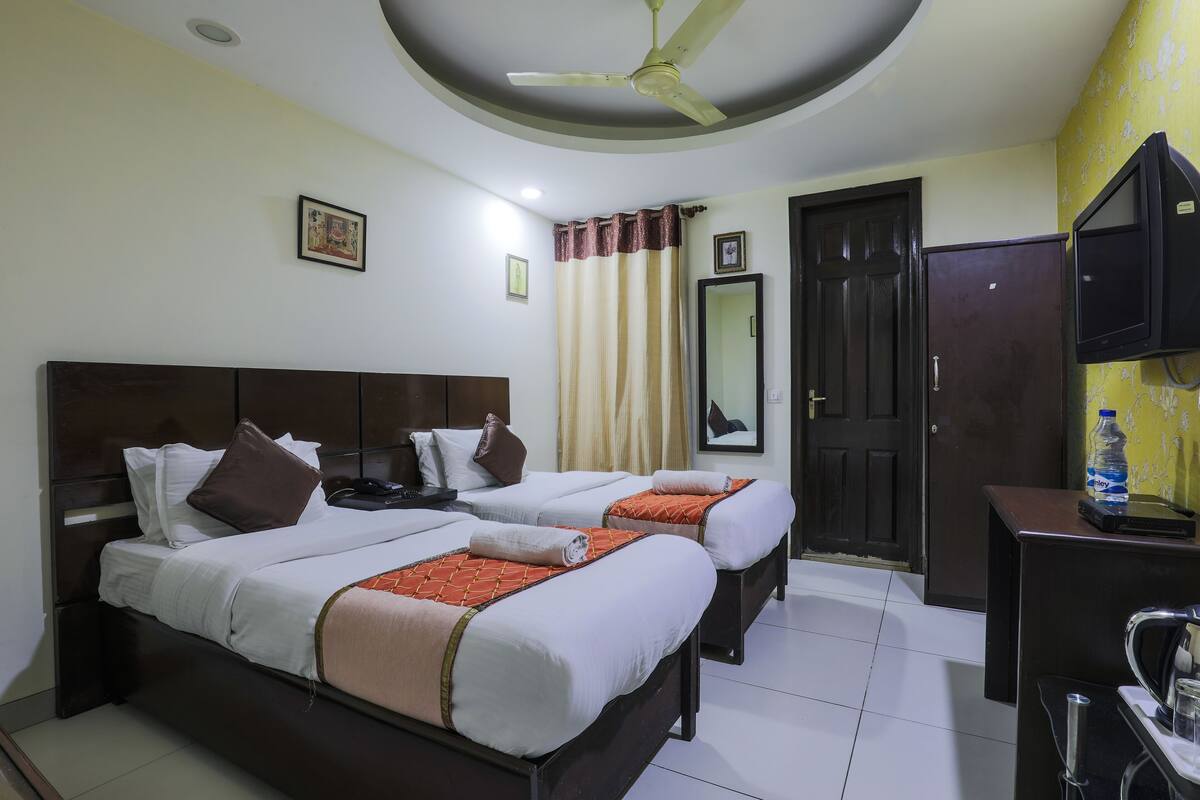 Camera d'albergo con due letti, una ventola a soffitto, una TV, un distributore d'acqua e una porta.