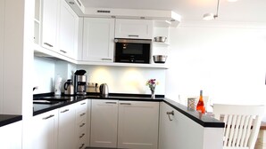 A modern kitchen with white cabinets, a black countertop, and a built-in microwave. - Die kleine Residenz (Sylt)