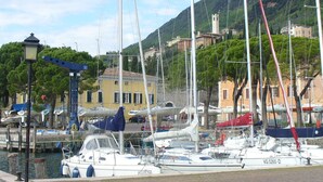 A marina with boats docked, a building with a yellow facade, and a mountainous backdrop. - House in the paradise garden above v. Gargnano for individuals u. Children (Gargnano)