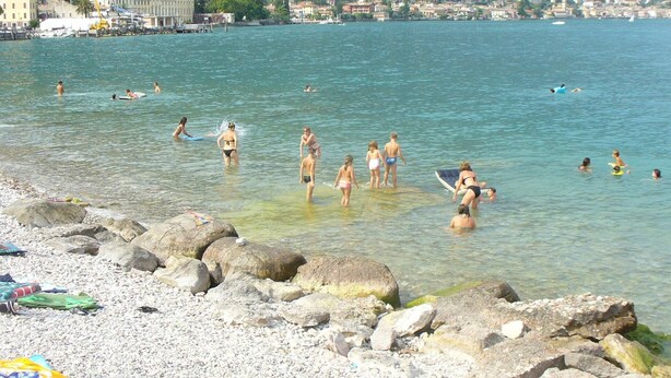 A beach with clear water, people swimming and sunbathing, and a rocky shoreline. - House in the paradise garden above v. Gargnano for individuals u. Children (Gargnano)