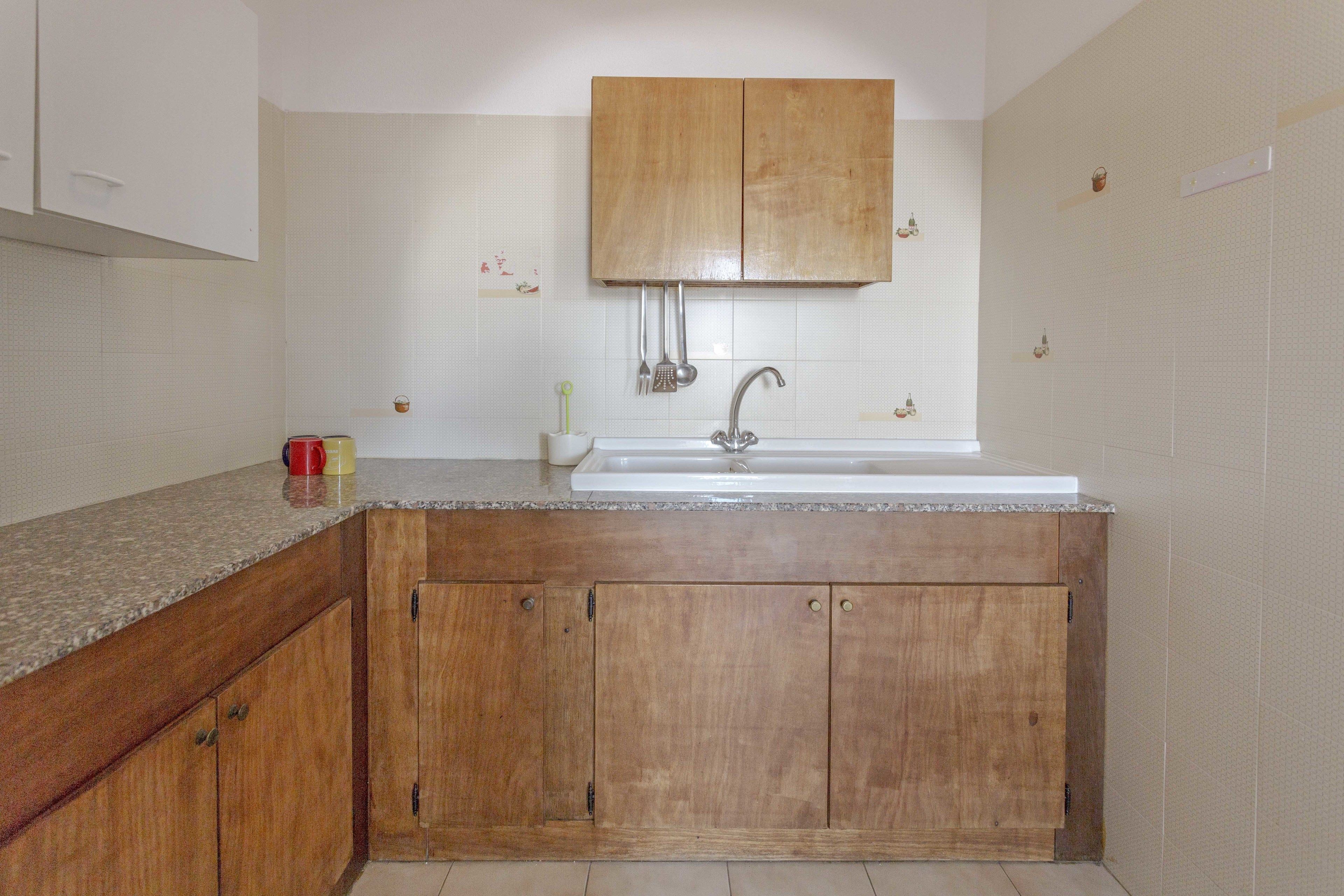 Een keuken met houten kastjes, een witte wasbak en een aanrecht.