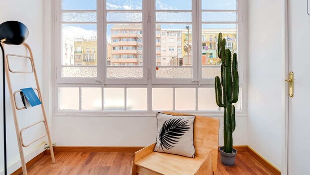 A room with a large window, a wooden chair, a cactus plant, and a ladder. - Sweett | Rocafort 104 (Barcelona)