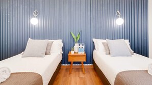 A hotel room with two beds, a small wooden nightstand with toiletries, and a blue curtain backdrop. - Sweett | Rocafort 104 (Barcelona)